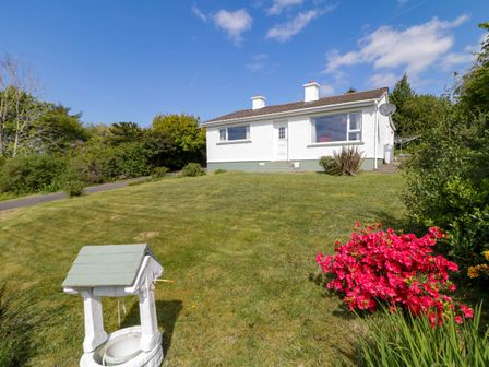 A white single story house with a green lawn and a small decorative well at LOCH ILLION VIEW in Dungloe County Donegal