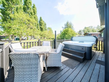 An outdoor deck with a table and four chairs and a hot tub at Lakeside Lullaby Billing Aquadrome Holiday Park