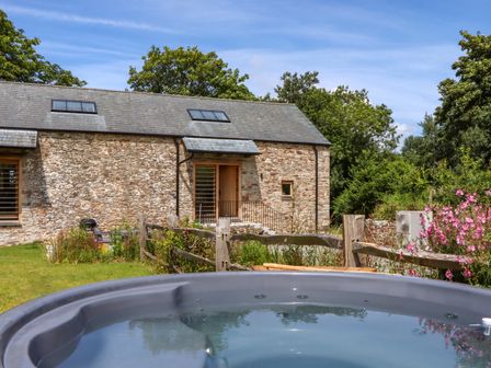 An outdoor area with a hot tub and a stone building at Lower Walreddon Barn in Tavistock