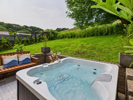 A hot tub with a bench and planters in a garden at 59a Gwscwm Road