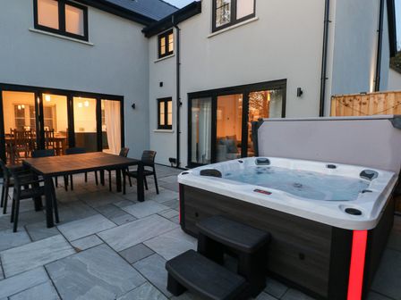 An outdoor patio with a hot tub and dining table at Ty Landsker Houghton near Neyland