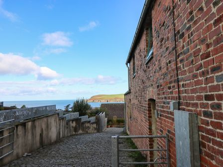 A pathway leading to a gate beside a brick wall overlooking the sea at The Barn in Newport