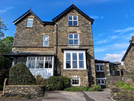 An exterior view of a stone building with windows and bushes at 1 Park Road Windermere