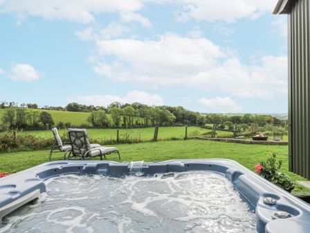 A hot tub with outdoor chairs and a green landscape at Brondel Luxury Shepherd's Hut in 