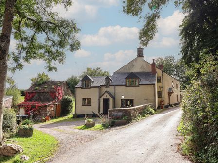 A cottage with a driveway and trees at Denhill Cottage in Chipstable near Wiveliscombe