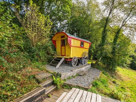 A gypsy caravan on a gravel base surrounded by trees and grass at Prudence Panson Mill near Ashwater