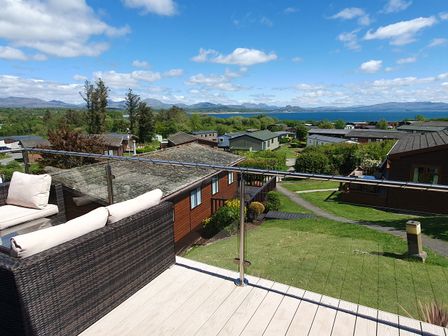 A balcony with a sofa overlooking houses and landscape at The Hideaway in Pwllheli