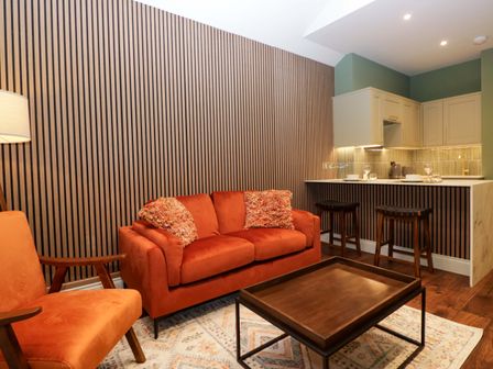 A living room with a sofa, armchair, coffee table, and kitchen counter at The Studio in Windermere