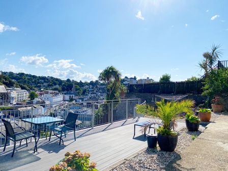 A garden with a table and chairs overlooking a view at Ockendon House Apartment B in Torquay