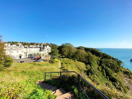 An outdoor area with a building next to the sea at Upper Stable - The Stables Apartments at Meadfoot Bay, Torquay