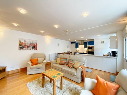 A living room with sofas and a kitchen area at Lower Stable - The Stables Apartments at Meadfoot Bay in Torquay