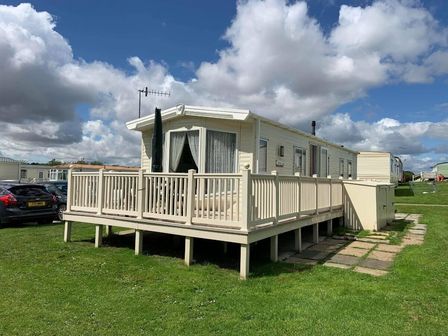 a mobile home with a deck and steps on a grassy area at Cayton Bay Caravan Park - Holiday Accommodation 11337 in Cayton