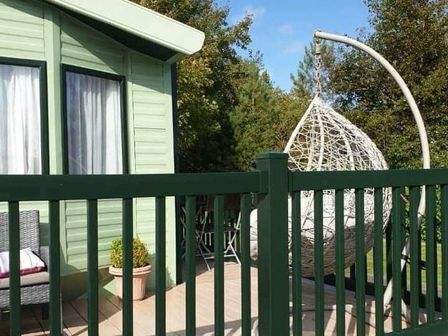 a deck with a hanging chair and a green railing at Hafan y Mor Haven - Holiday Accommodation 11370 in Pwllheli