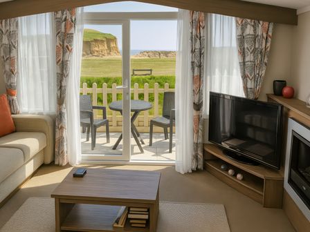 a living room with a TV, coffee table, and view of a patio at Freshwater Beach Holiday Park - Holiday Accommodation 12281 in Burton Bradstock