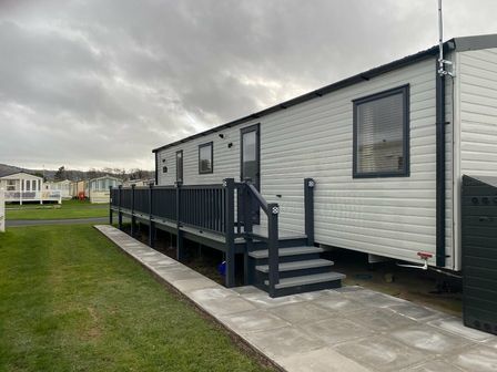 a caravan with a deck and steps on a grassy area at Lido Beach Holiday Park - Holiday Accommodation 12350, Prestatyn