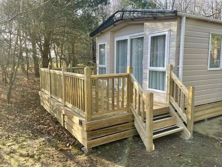 a holiday home with a wooden deck and steps surrounded by trees at Kelling Heath Holiday Park - Holiday Accommodation 12919 in Holt