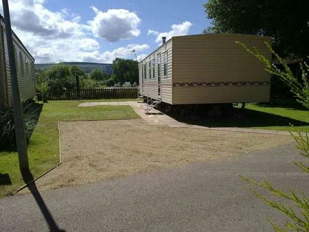 a static caravan situated on a gravel area with grass and trees at Butlins Minehead - Holiday Accommodation 13397, Minehead