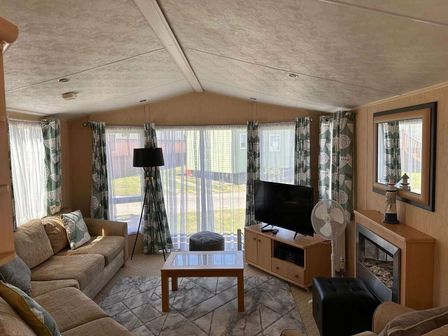 a living room with a sofa, coffee table, television, and large windows at Aberystwyth Holiday Village - Holiday Accommodation 13768, Aberystwyth