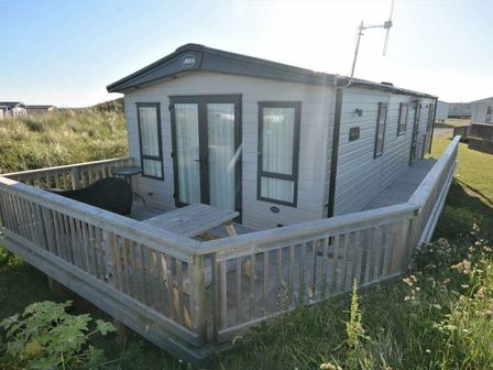 a caravan with a wooden deck and picnic table at Perran Sands - Holiday Accommodation 14626 Perranporth