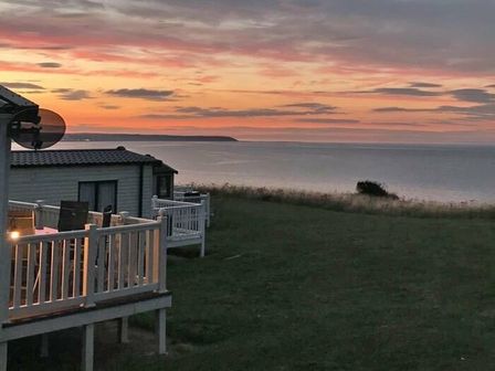 a view of the sea at sunset with two holiday homes in the foreground at Reighton Sands Holiday Park - Holiday Accommodation 15175, Filey