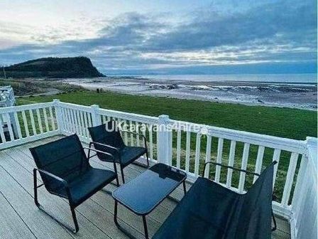 a deck with chairs and a table overlooking a beach and grassy area at Craig Tara Holiday Park - Holiday Accommodation 15296, Ayr