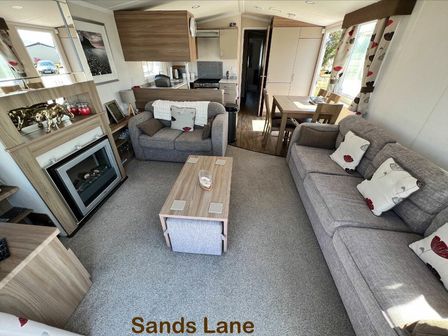 a living room with two sofas, a table, and an electric fireplace at Greenacres Holiday Park - Holiday Accommodation 15540 Porthmadog