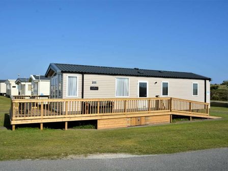 a mobile home with a wooden deck located in a grassy area at Perran Sands - Holiday Accommodation 15554, Perranporth
