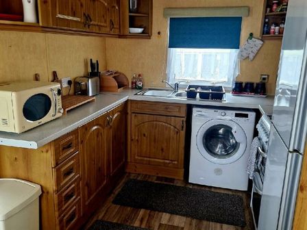 a kitchen with wooden cabinets, a sink, a washing machine, and a microwave at Clarach Bay Holiday Village - Holiday Accommodation 15868, Aberystwyth