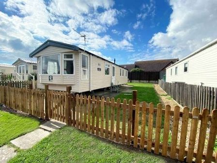 a mobile home with a fenced yard and cloudy sky at Unity Holiday Resort - Holiday Accommodation 15970 in Brean Sands