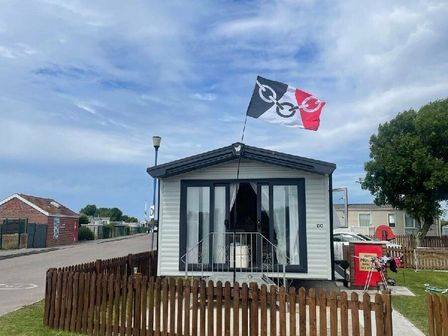 a holiday home with a flag on the roof and a wooden fence at Unity Holiday Resort - Holiday Accommodation 16079 Burnham-on-Sea