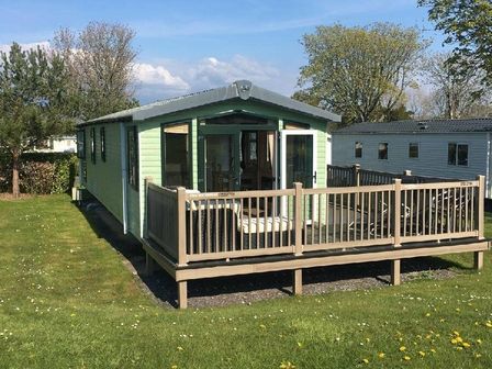 a holiday cabin with a deck, surrounded by grass and trees at Hafan y Mor Haven - Holiday Accommodation 16255, Pwllheli