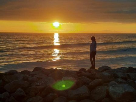 a person standing on rocks by the beach at sunset with water reflections at Lyons Sunnysands Holiday Park - Holiday Accommodation 16276 Talybont