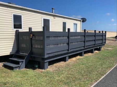 a fenced outdoor deck area next to a mobile home at Tingdene North Denes Caravan Park - Holiday Accommodation 16568 in Lowestoft