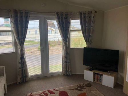 a living room with curtains and a television at Lido Beach Holiday Park - Holiday Accommodation 16964, Prestatyn