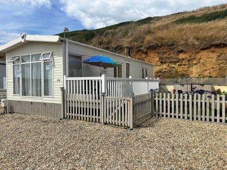 A mobile home with a deck and fence at Freshwater Beach Holiday Park - Holiday Accommodation 17116 in Burton Bradstock near Bridport