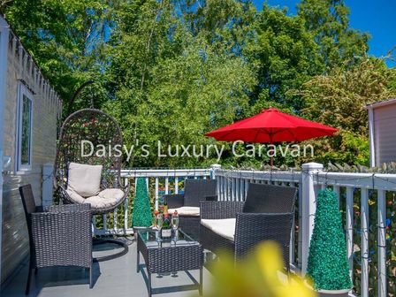 a terrace with a hanging chair, outdoor seating, and an umbrella at Daisy's Luxury Caravan in Tattershall