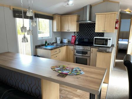 a kitchen with cabinets, stove, and dining table at Marsh Farm Holiday Park - Holiday Accommodation 17642 in Great Yarmouth