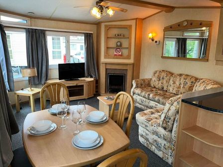 a living room with a sofa, dining table, television, and fireplace at Marsh Farm Holiday Park - Holiday Accommodation 17742 in Great Yarmouth