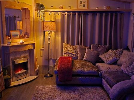 a cozy living room with a sectional sofa, floor lamp, and an electric fireplace at Hafan y Mor Haven - Holiday Accommodation 18358, Pwllheli