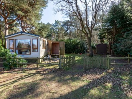 a cabin with a porch surrounded by trees and grass at Kelling Heath Holiday Park - Holiday Accommodation 18663 in Holt