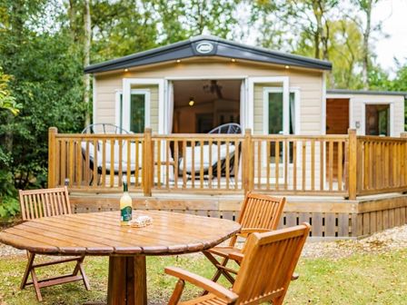 a wooden outdoor table with chairs and a holiday accommodation with large windows at Kelling Heath Holiday Park - Holiday Accommodation 18664, Holt