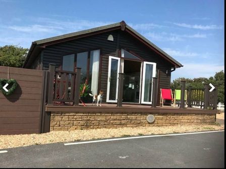 a wooden holiday cabin with a deck and a dog outside at Port Haverigg Holiday Village - Holiday Accommodation 19115, Millom