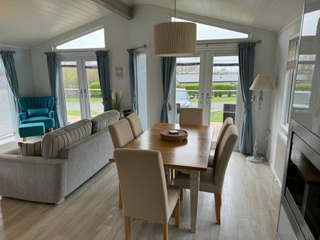 a dining area with a wooden table and chairs next to a living area with a sofa at Hafan y Mor Haven - Holiday Accommodation 19472 in Pwllheli