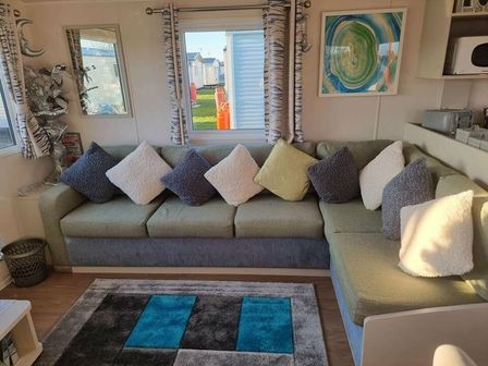 a living room with a green and gray couch and decorative pillows at Cala Gran Holiday Park - Holiday Accommodation 19633, Fleetwood