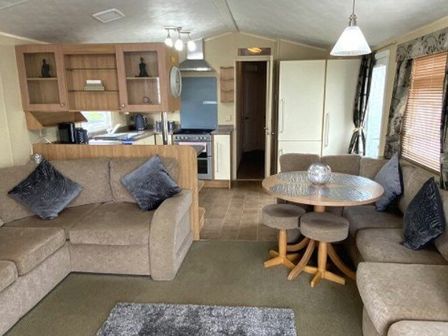 a living room with a sofa, round table, and kitchen area at Quay West Holiday Park - Holiday Accommodation 19725 in Ceridigion