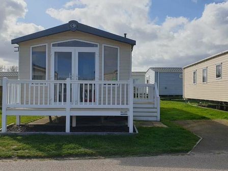 a holiday home with a deck and grass in front at Caister Holiday Park - Holiday Accommodation 19783 Caister