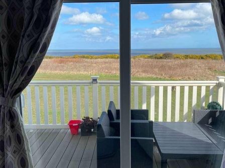 a view from a balcony overlooking a grassy area and the sea at Reighton Sands Holiday Park - Holiday Accommodation 20234 in Filey