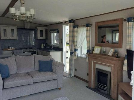 a living room with a gray sofa, a coffee table, and a kitchen area at Ty Mawr Holiday Park - Holiday Accommodation 20399, Abergele