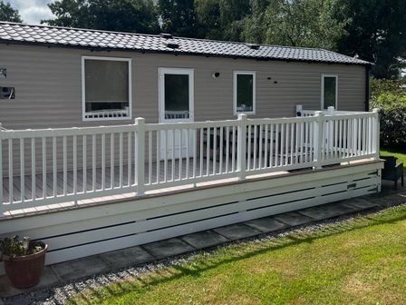 A mobile home with a deck and railing at Hafan y Mor Haven - Holiday Accommodation 20548 Pwllheli