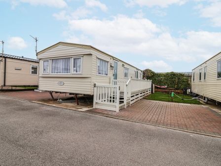 A static caravan with a decking area and paved driveway at Golden Gate Holiday Centre - Holiday Accommodation 20618 Abergele